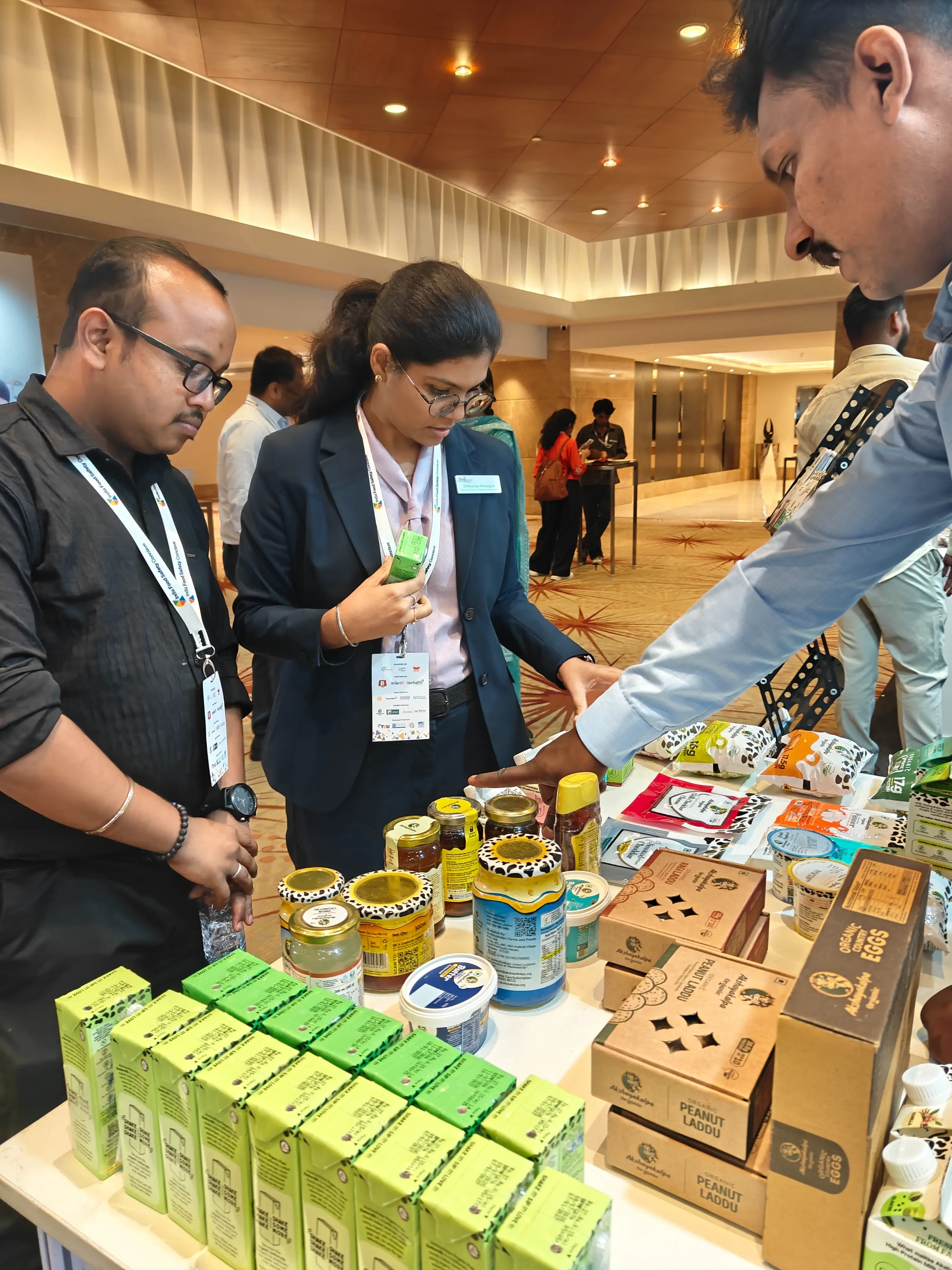 Conference delegates examining a display table of packaged food and beverage products.