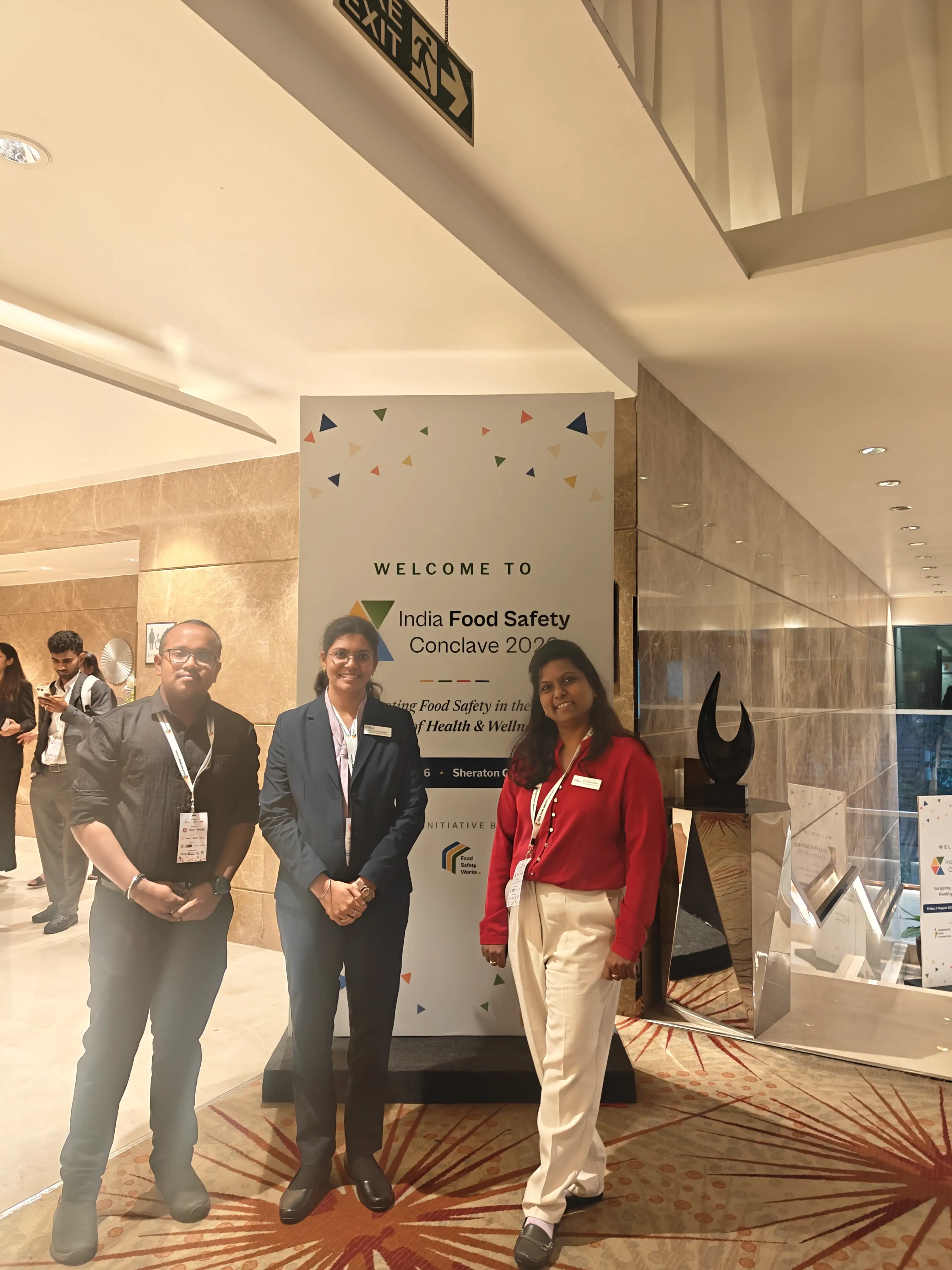 Delegates standing beside the welcome signage at the entrance of a food safety conference venue.